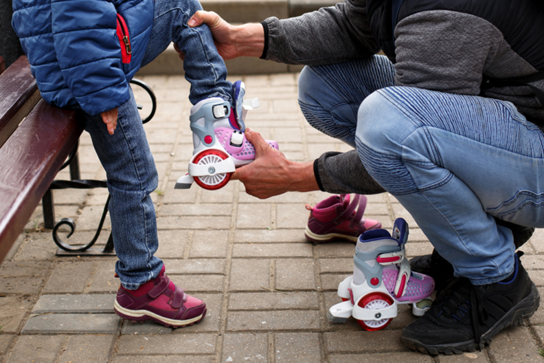 Photograph of an adult helping a child put on rollerblades