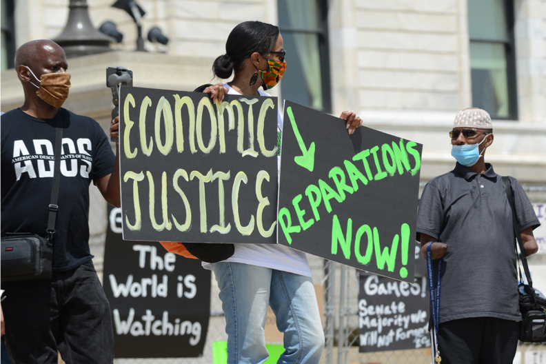 Reparations Protest with a protestor holding signs that read: Economic Justice now, Reparations now
